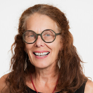 Frau mit lockigem Haar und Brille, offen lächelnd.